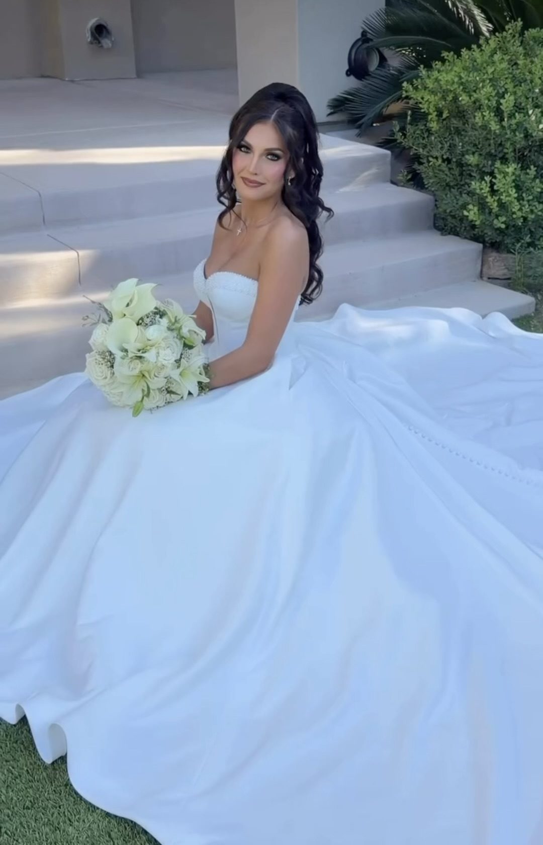 Las Vegas bride seated on stone steps with her wedding dress train spread out around her, holding a white bouquet of calla lilies, roses and lilies