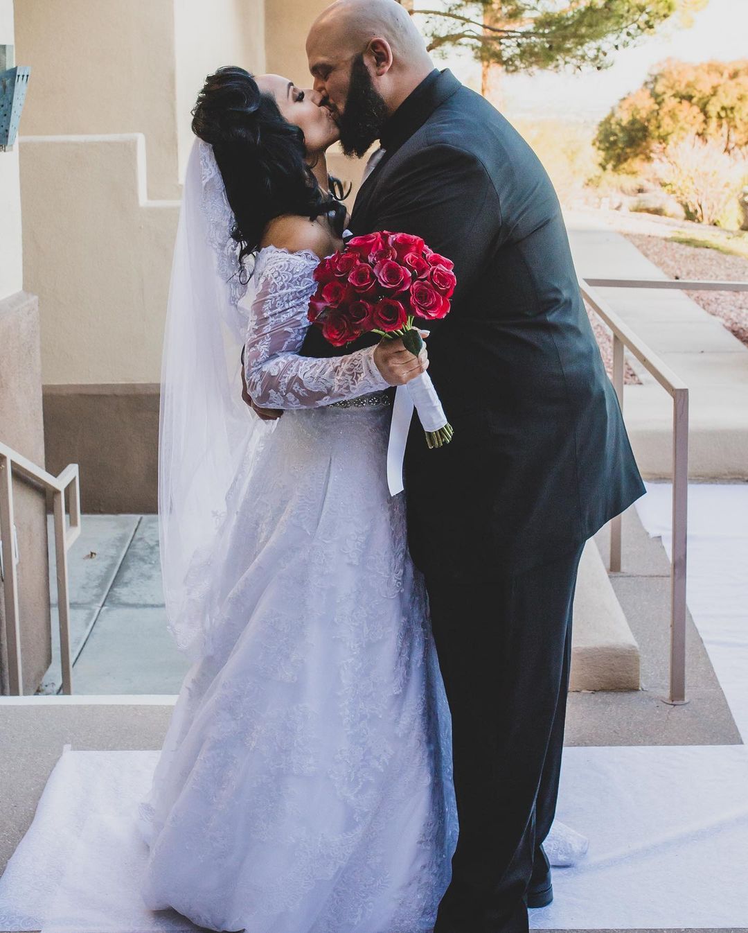 Bride holding a red rose bouquet kissing the groom on the steps at a Las Vegas wedding