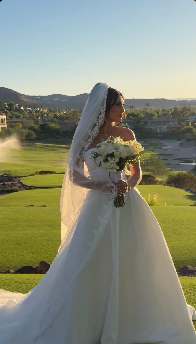 Las Vegas bride in a lace-edged veil holding a white lily and rose bouquet on a golf course at golden hour
