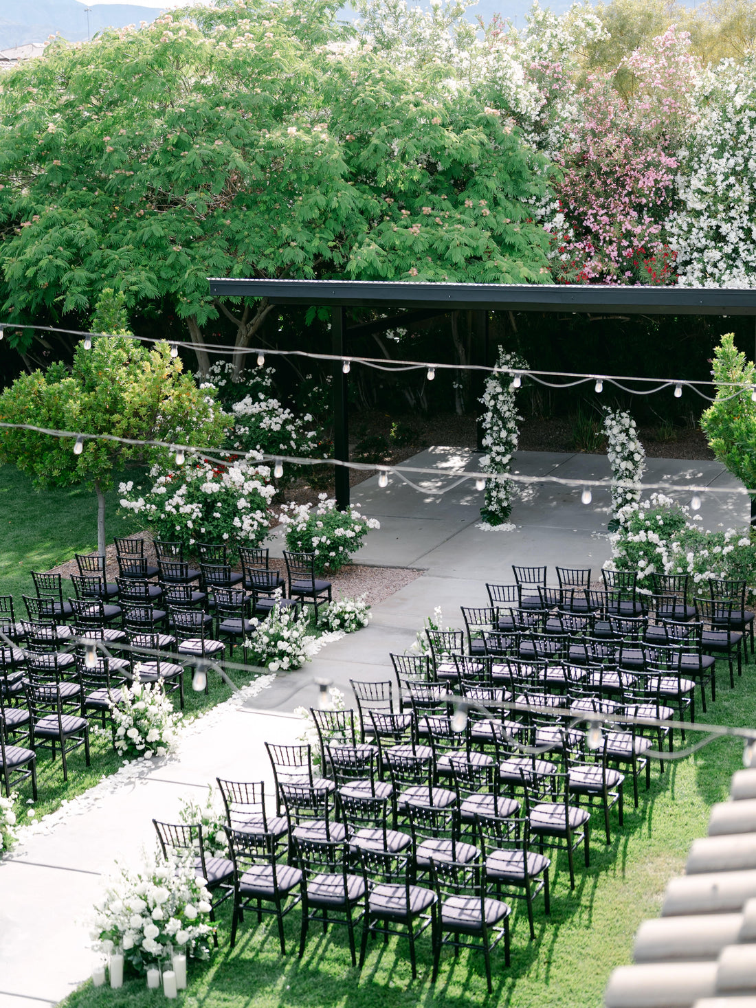 Garden wedding ceremony setup in Las Vegas with black chiavari chairs, white aisle flowers and floral ceremony pillars