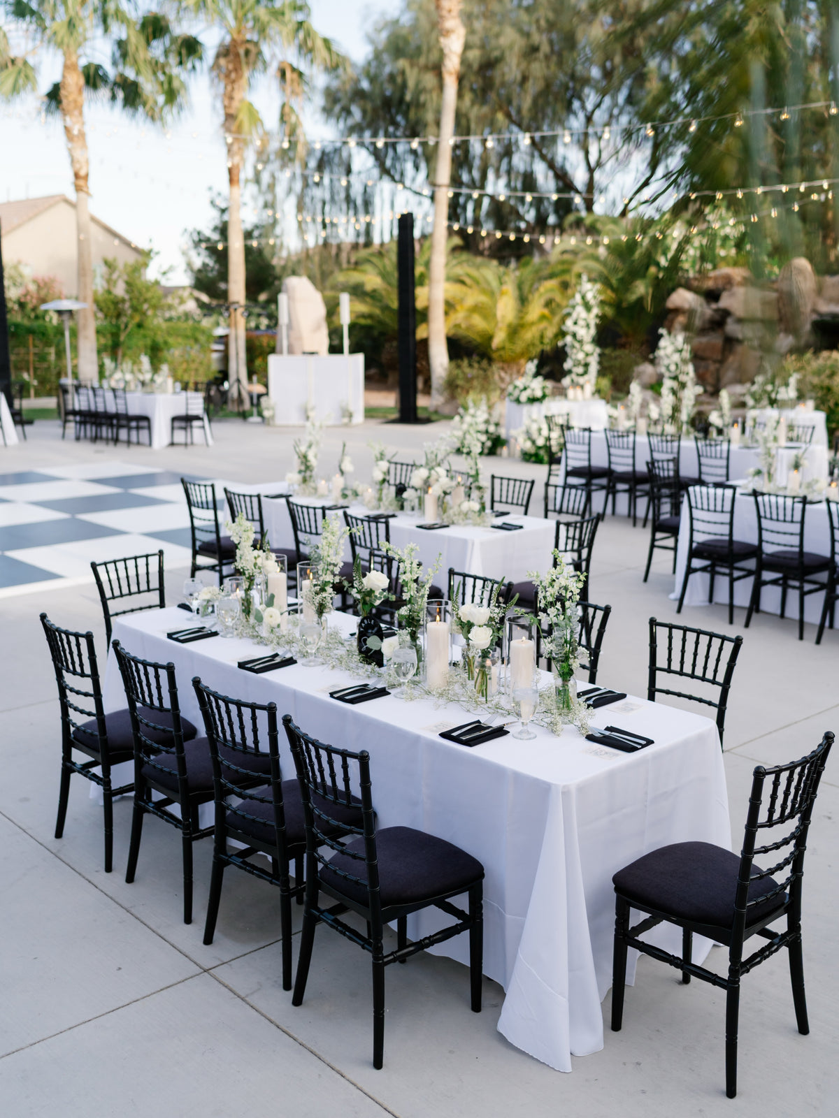 Outdoor Las Vegas wedding reception with white floral centerpieces, candles and black chiavari chairs under string lights