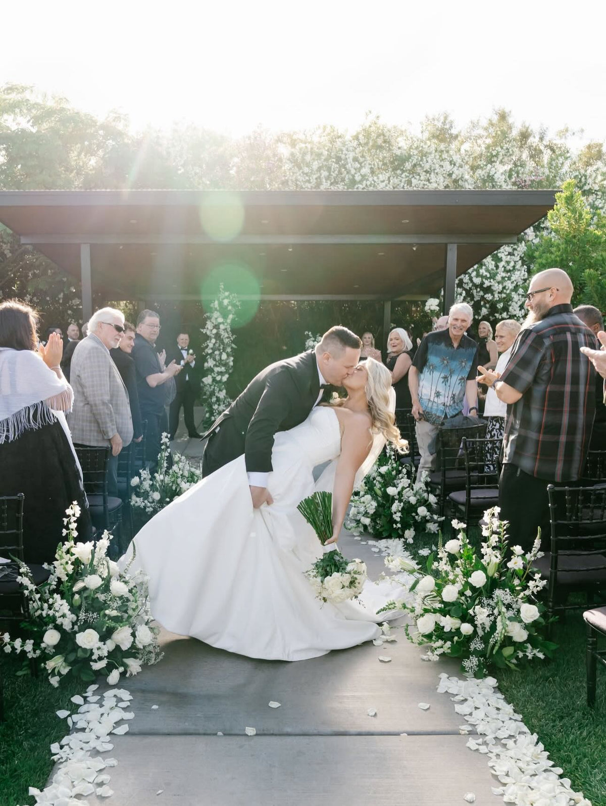 Groom dipping the bride for a kiss in the ceremony aisle lined with white flowers and rose petals in Las Vegas