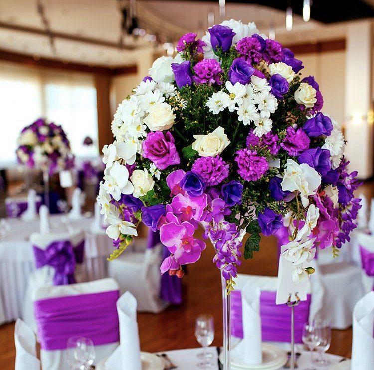Tall wedding centerpiece of purple orchids, roses and lisianthus on a reception table with purple chair sashes in Las Vegas